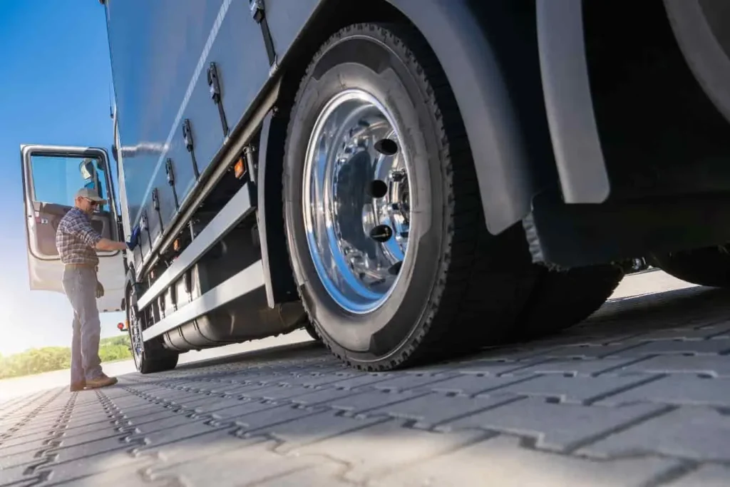 Un homme se penche pour vérifier la pression d'un pneu de remorque, illustrant un contrôle technique essentiel avant de prendre la route.