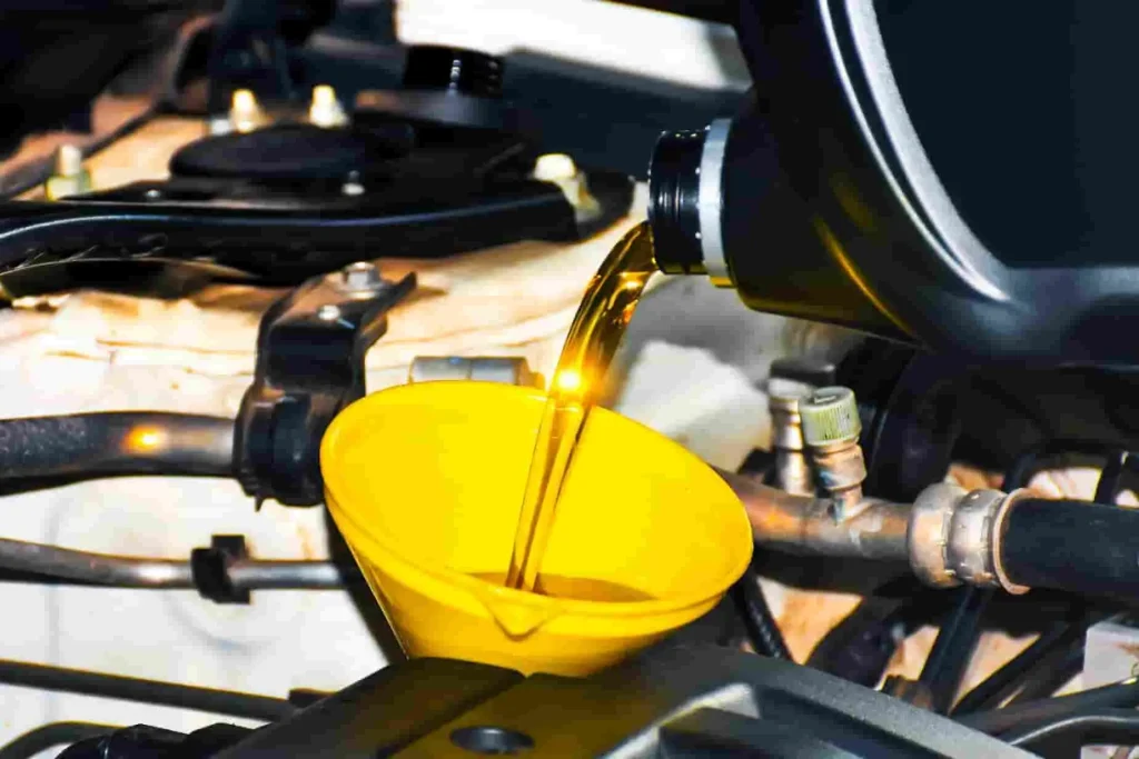 Huile versée dans moteur via entonnoir jaune, image illustrant une étape de vidange boîte automatique dans le compartiment moteur