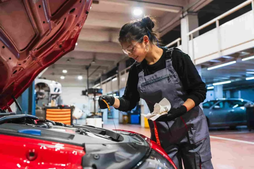 Mécanicien vérifiant le niveau d’huile moteur sur voiture rouge, image illustrant une étape de vidange boîte automatique en atelier