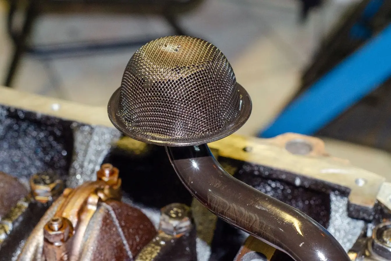 Crépine d'huile moteur en maille métallique fixée au tuyau de ramassage, visible dans le carter d'huile du moteur.