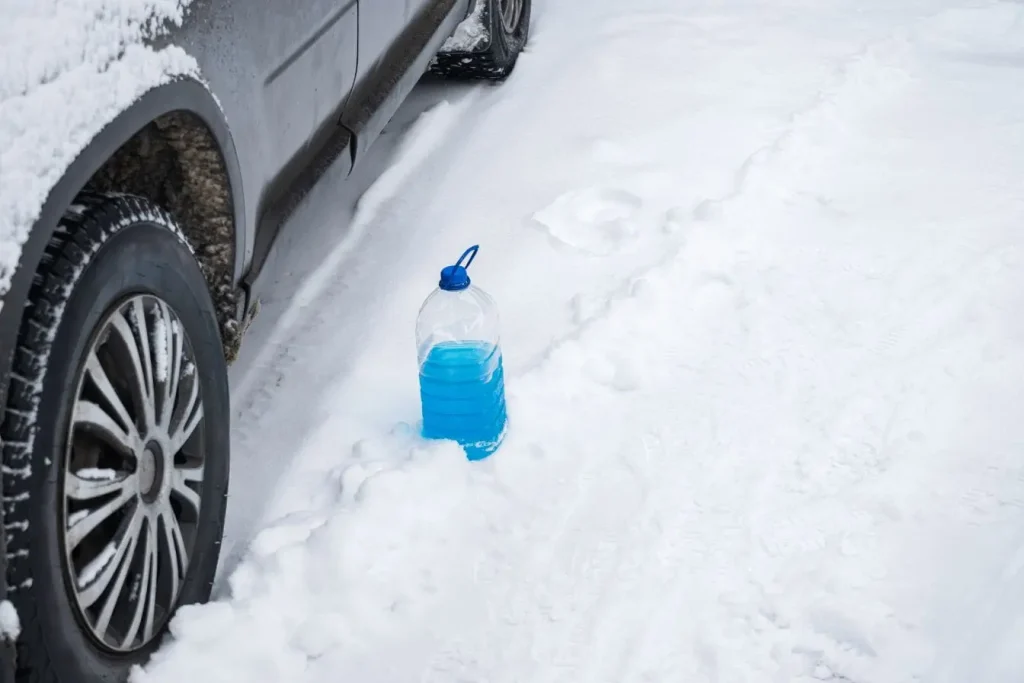 Bidon de liquide lave-glace bleu posé dans la neige, image reflétant l’importance de l’entretien automobile en conditions hivernales