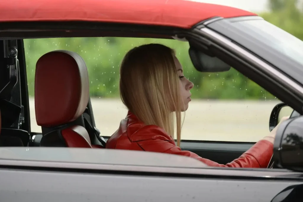 Conductrice assise dans une voiture rouge, image illustrant les dangers de la conduite sous fatigue et la baisse de vigilance au volant.