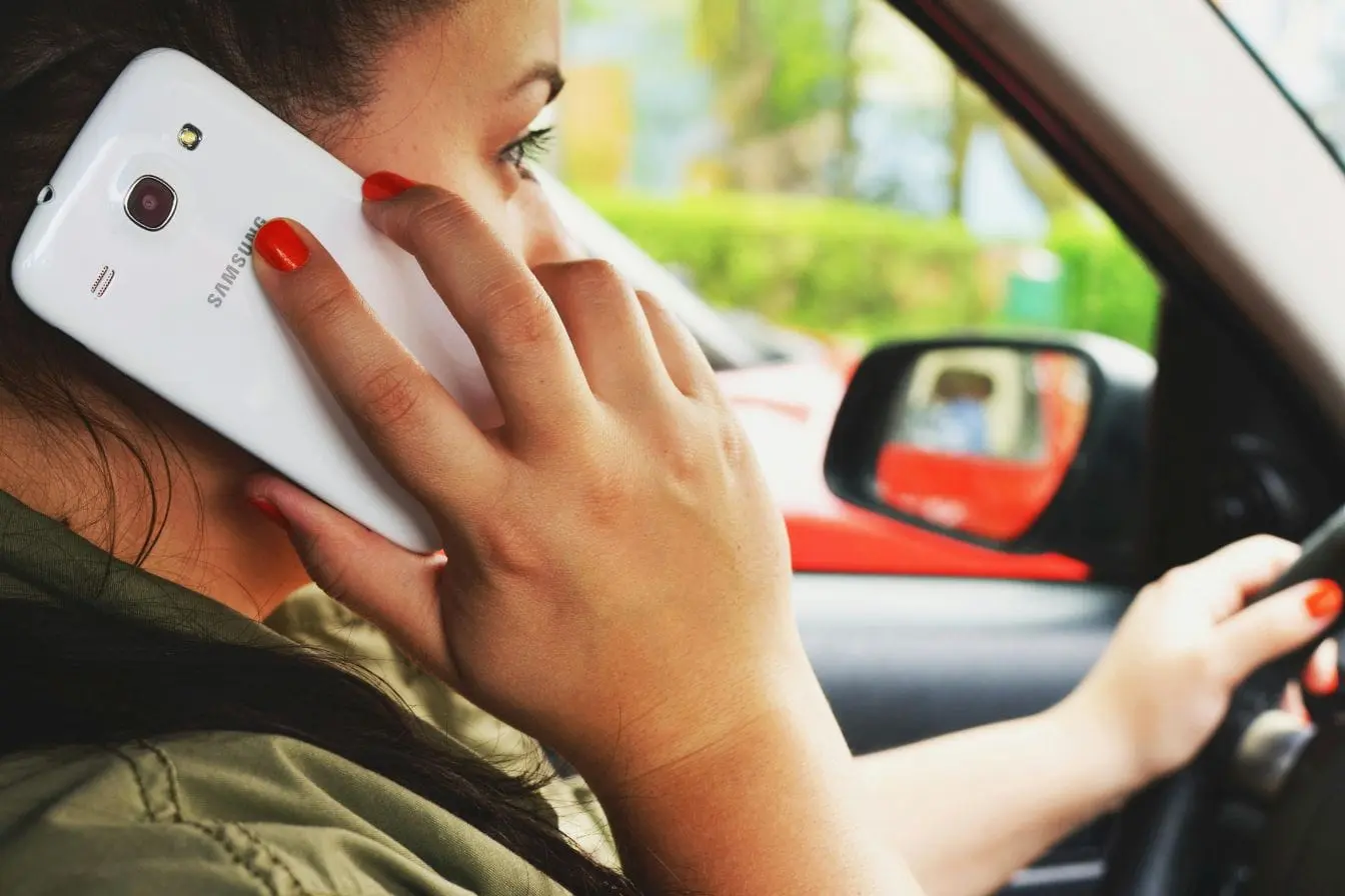 Conductrice tenant smartphone à l’oreille en conduisant, image illustrant le téléphone au volant et les sanctions prévues avec retrait de points en 2026.