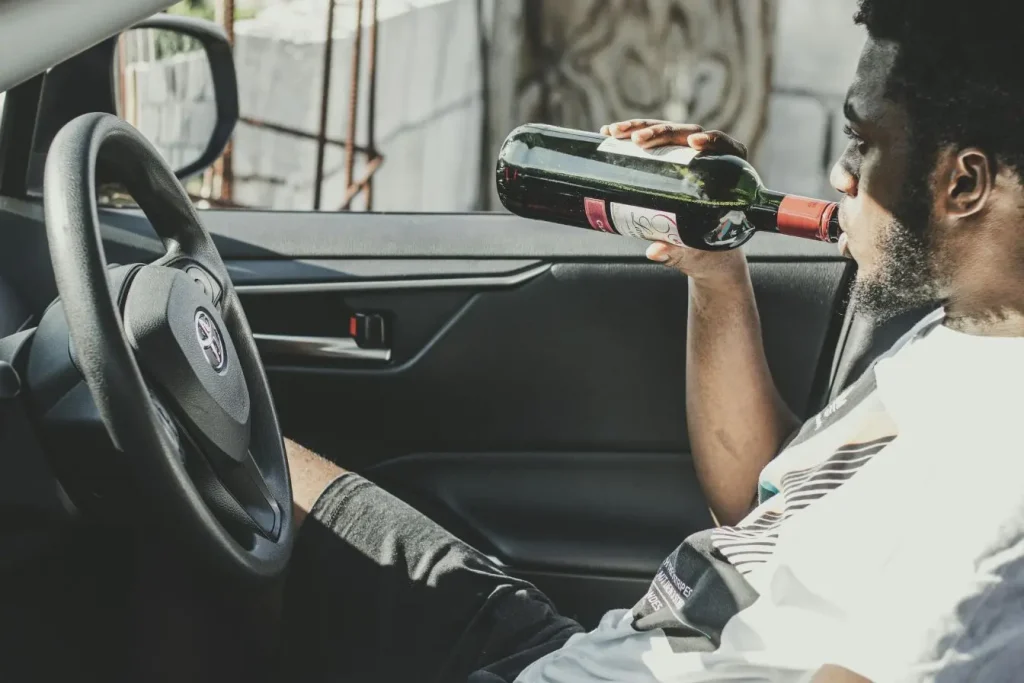 Conducteur assis au volant tenant bouteille de vin, image illustrant le danger de l’alcool au volant.