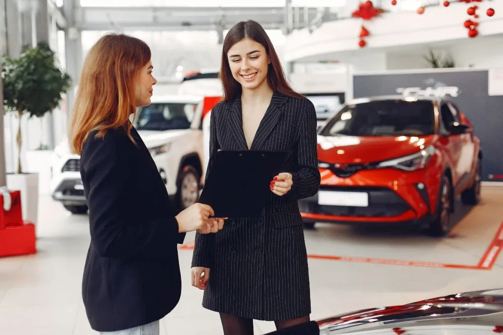 Deux personnes discutent dans un showroom automobile devant voitures exposées, image évoquant la vérification d’un certificat de non‑gage lors d’une vente.