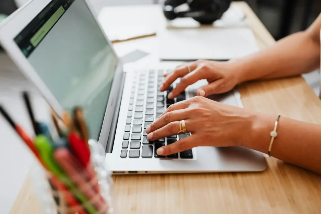 Mains tapant sur ordinateur portable illustrant la procédure en ligne pour demander un duplicata de carte grise via les démarches administratives numériques.