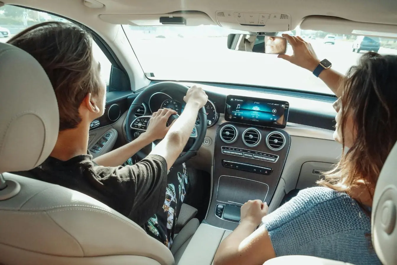 Conducteur tenant le volant avec passager ajustant miroir, image illustrant la transition du permis auto au manuel et l’apprentissage pratique.