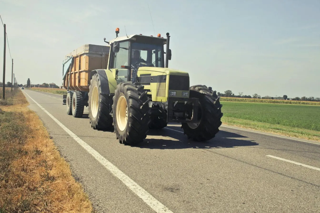 tracter une remorque Tracteur agricole vert tirant une remorque sur route rurale, image illustrant la nécessité d’un permis adapté pour tracter une remorque en toute sécurité.