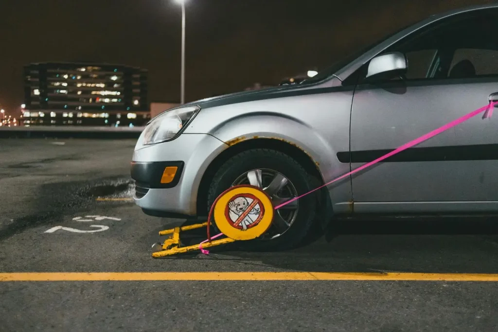 Voiture argentée immobilisée par un sabot jaune, image évoquant le stationnement sur trottoir sanctionné pour non-respect des règles de circulation urbaine.