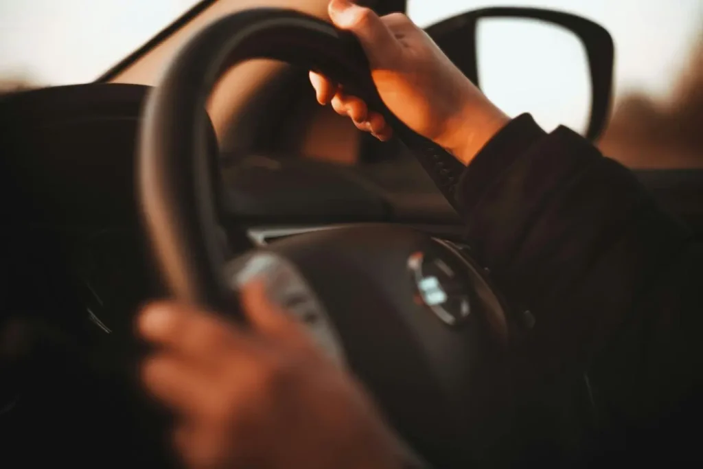 Mains serrant volant au coucher du soleil, image illustrant la conduite accompagnée et l’apprentissage progressif de la maîtrise routière.