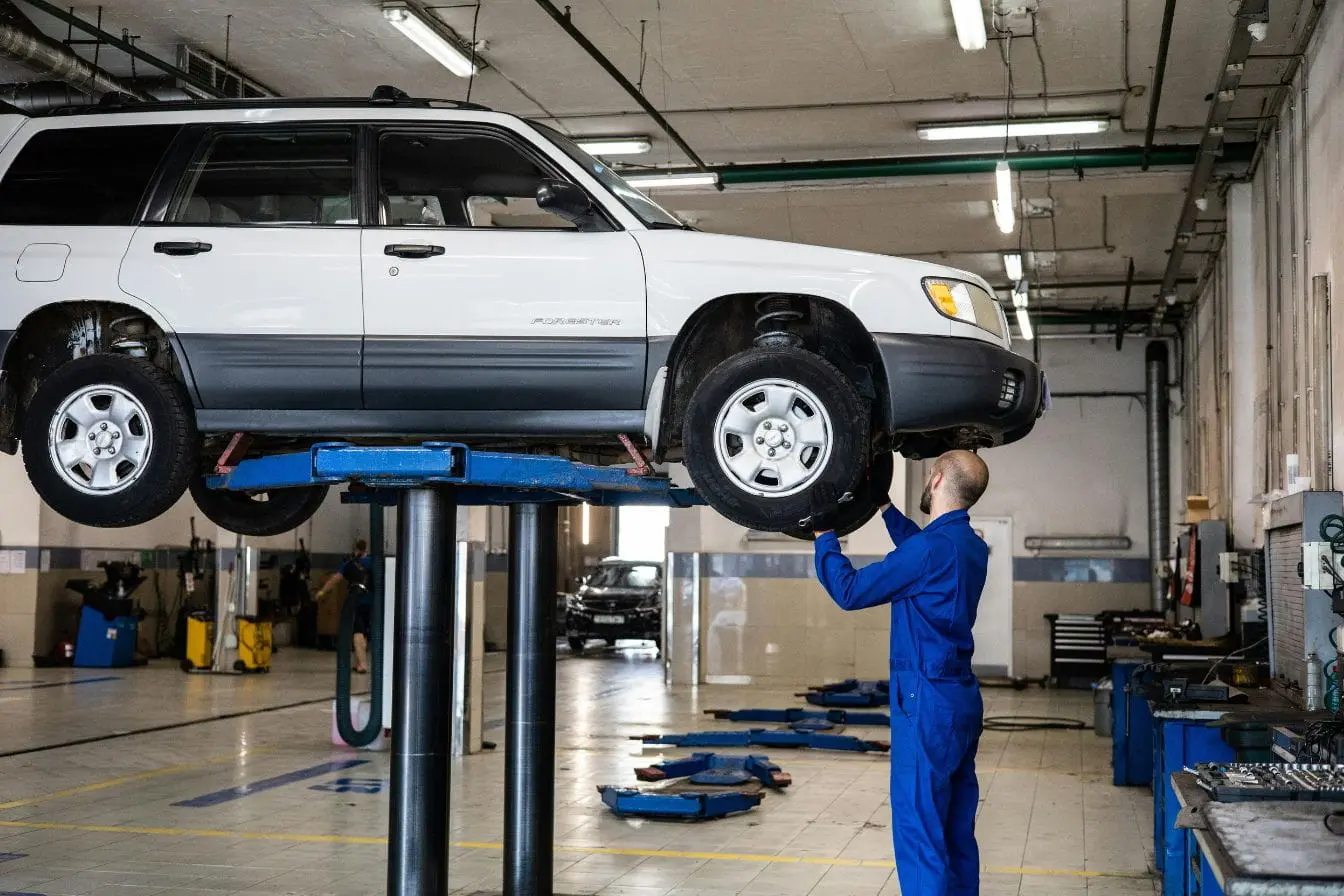Atelier automobile SUV blanc levé sur pont hydraulique avec mécanicien en bleu, image illustrant le comparatif des frais d’entretien électrique et thermique.