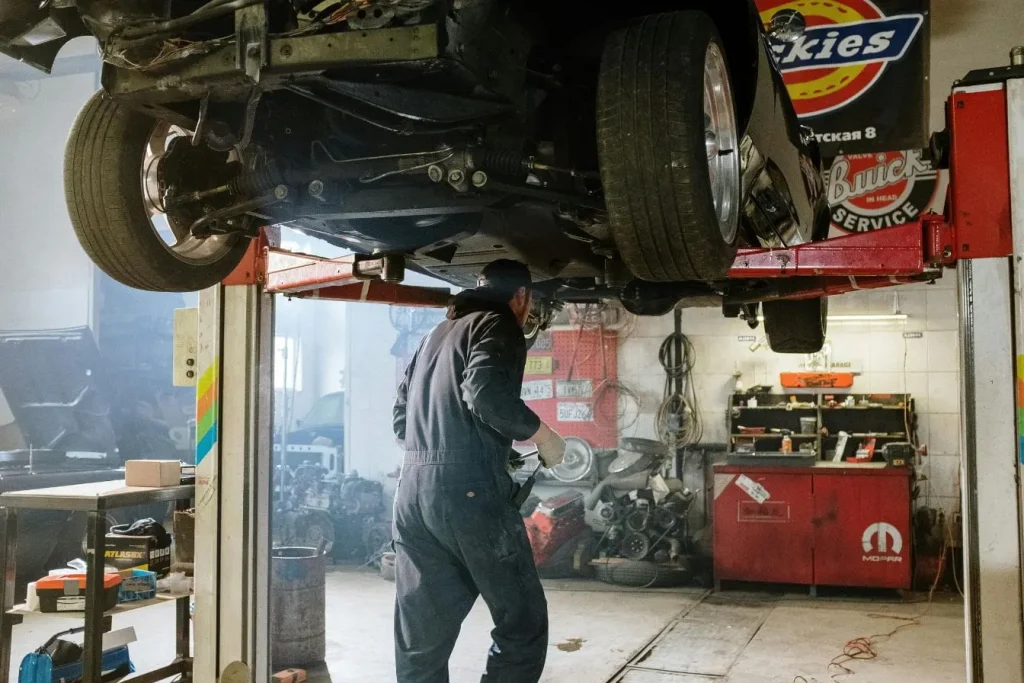 Mécanicien inspectant le dessous d’une voiture levée sur pont hydraulique, illustrant une suspension pneumatique en panne nécessitant réparation.