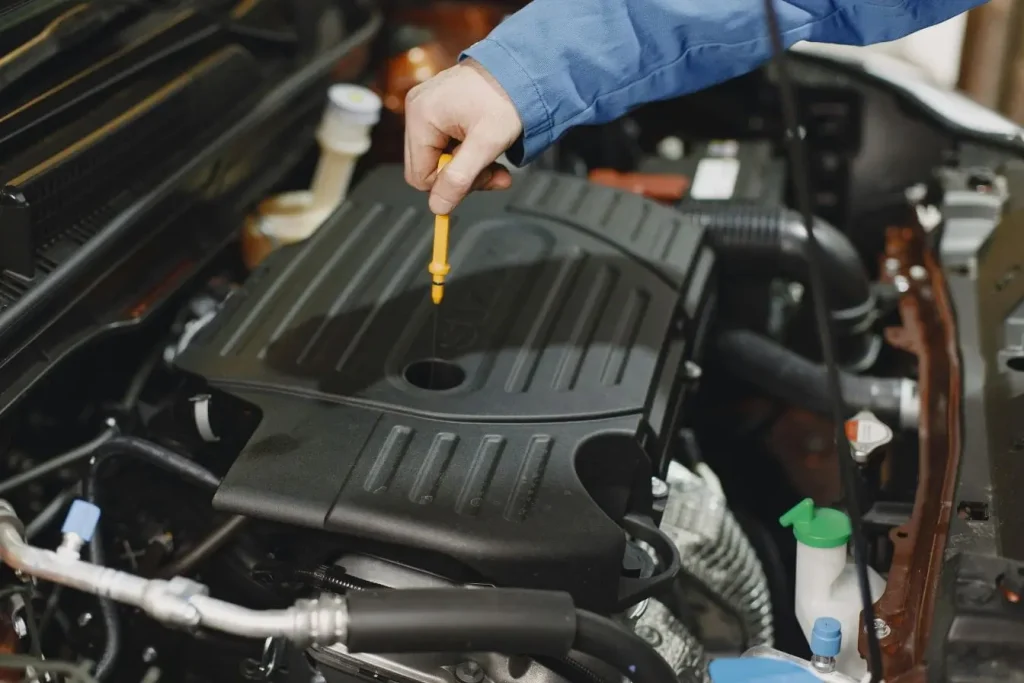 Gros plan moteur ouvert, une main tient une jauge jaune, image pratique pour comprendre la vérification et l’appoint du liquide de frein.