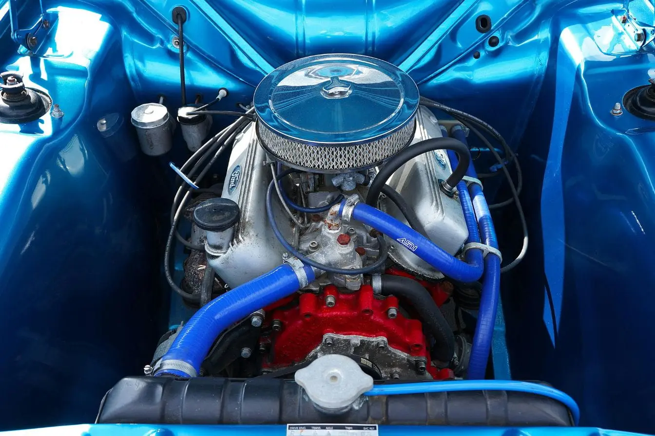Gros plan sur moteur avec durites bleues et pompe à eau, image évoquant les signes de défaillance à surveiller pour éviter une surchauffe.