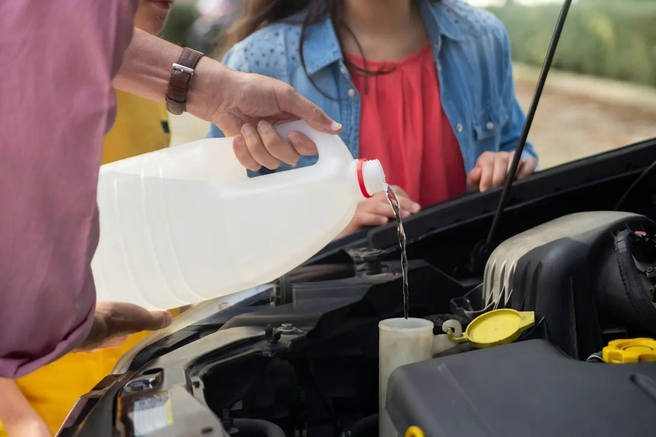 Gros plan sous capot, un conducteur verse du liquide dans le réservoir, illustrant la vérification et l’appoint du niveau de liquide de frein.