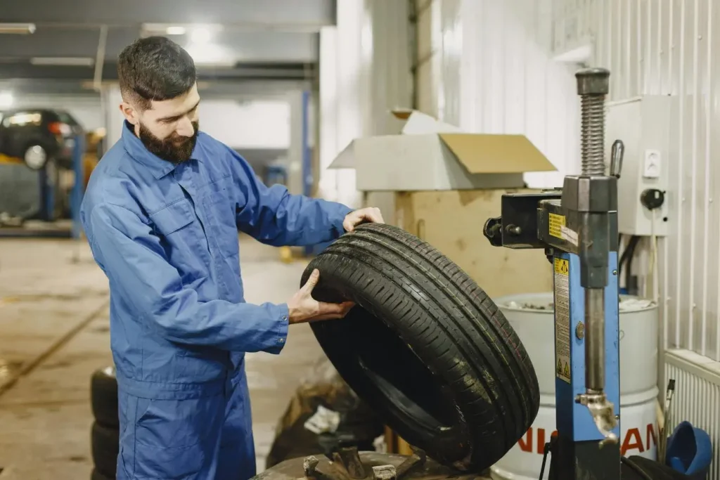 Mécanicien en bleu de travail inspectant pneu dans atelier, image illustrant la pratique des pneus rechapés pour prolonger leur durée de vie.
