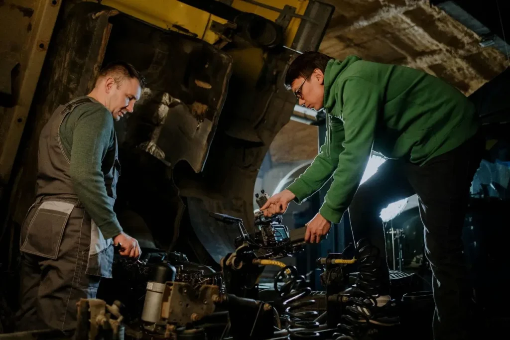 Deux personnes penchées sur machine dans atelier, image illustrant le remplacement d’un injecteur diesel avec expertise mécanique et collaboration.