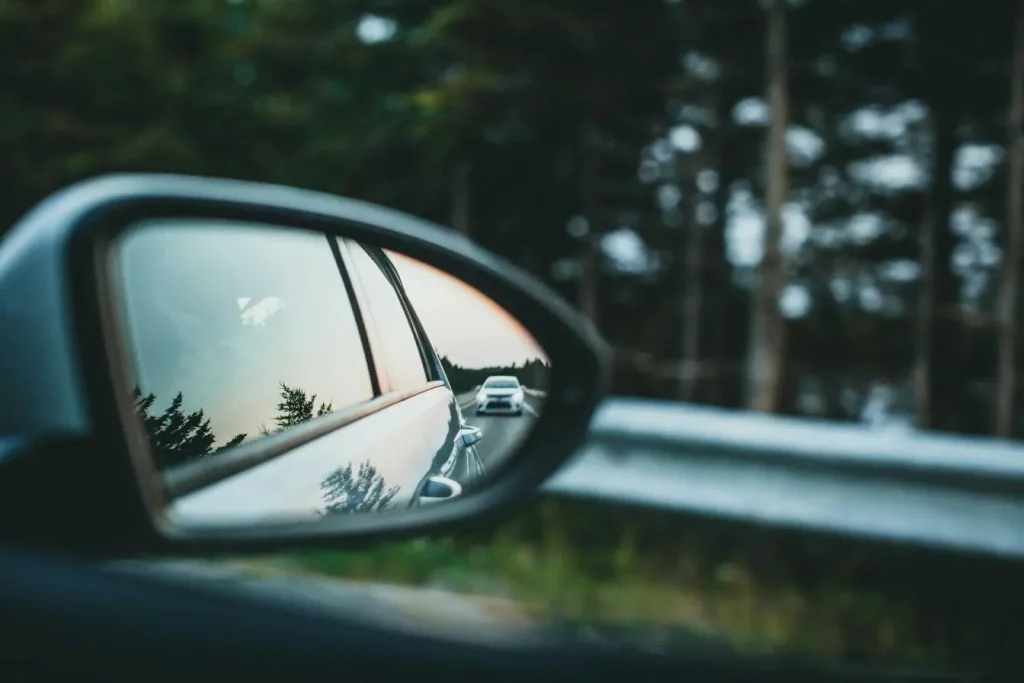 Vue d’un rétroviseur reflétant une voiture derrière traduisant la nécessité de savoir réagir en cas de rétroviseur extérieur cassé.