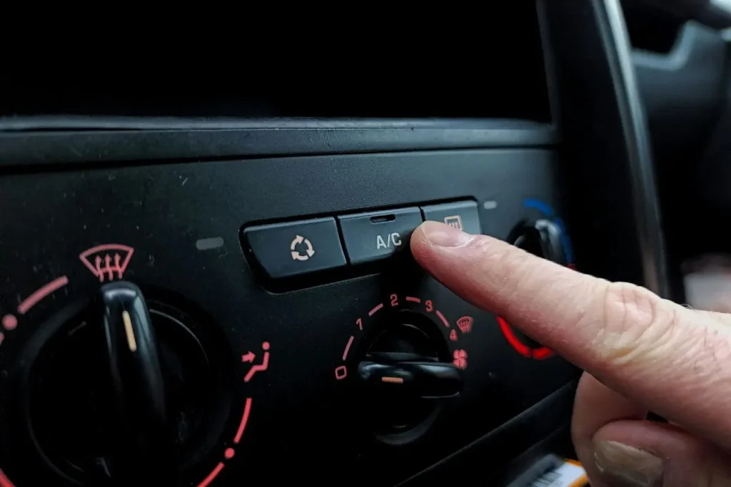 Doigt activant la climatisation sur panneau central, représentant l’entretien de la climatisation de voiture.