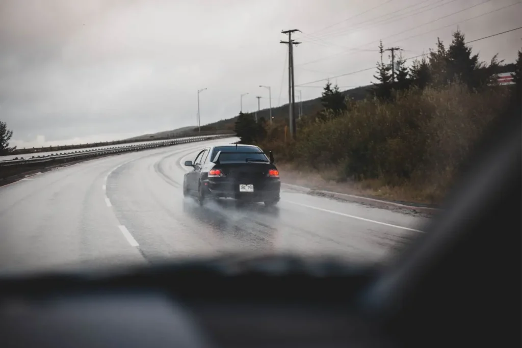 Voiture noire roule sur route mouillée, image illustrant la conduite au Maroc avec permis français et respect des règles de sécurité par temps de pluie.