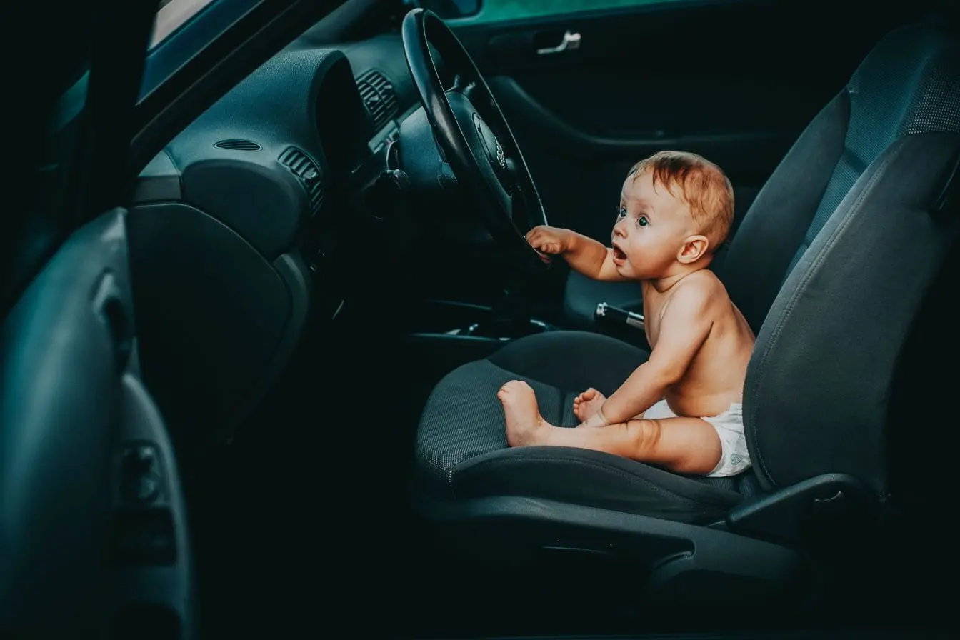 Bébé assis sur siège conducteur Bébé assis sur siège conducteur en couche, image illustrant les dangers mortels liés à la chaleur quand un enfant est oublié dans une voiture.