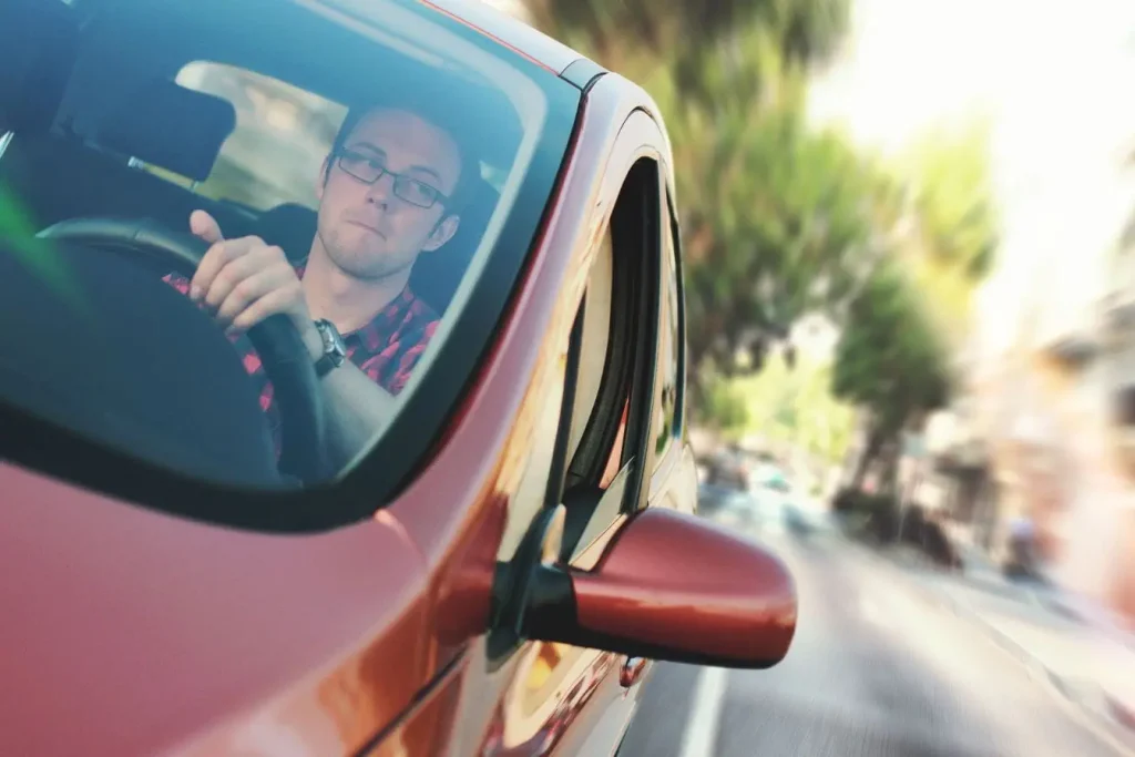 Conducteur en chemise à carreaux rouges, lunettes au visage, volant tenu fermement, image qui illustre les conditions de vue nécessaires pour le permis.