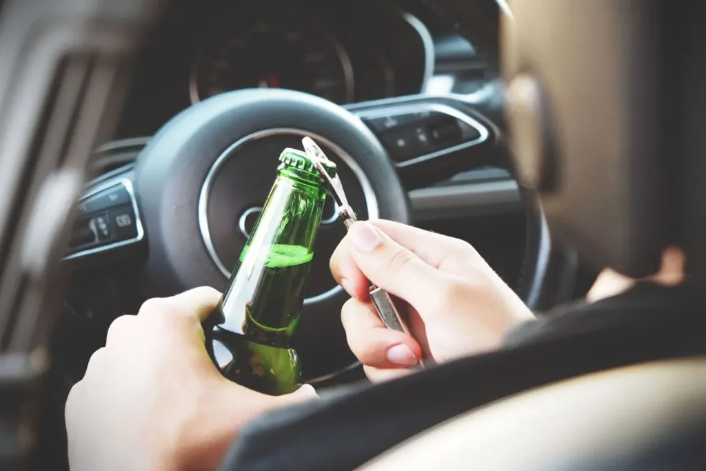 Conducteur ouvrant une bouteille dans une voiture, image qui illustre les dangers liés au non-respect du taux d’alcoolémie légal en Europe.