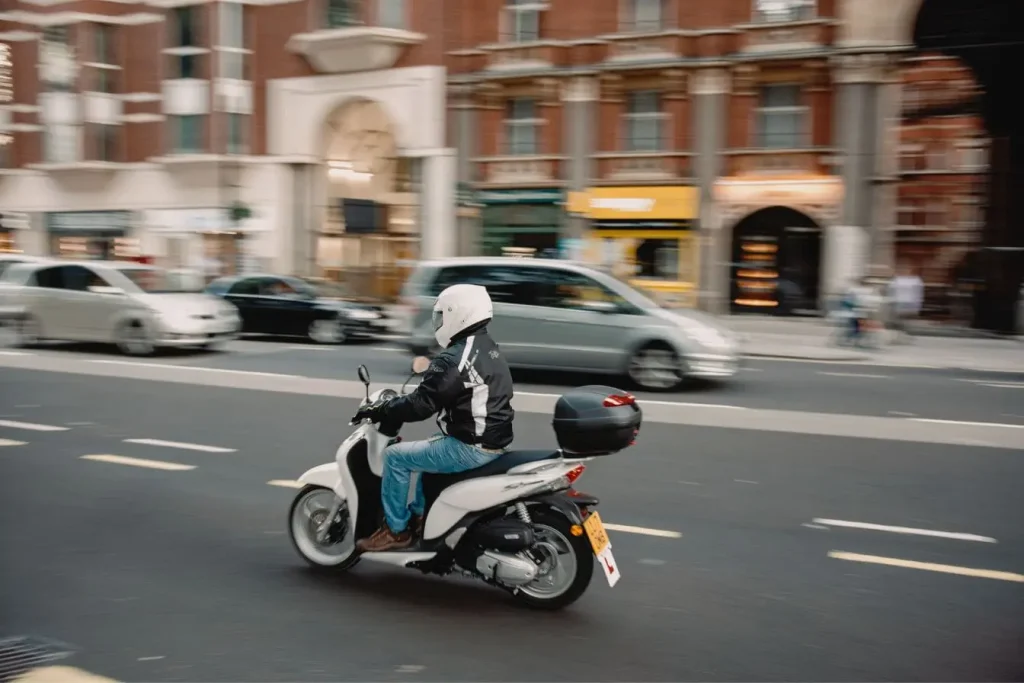 Conducteur en jeans et casque blanc sur scooter, illustration de la formation pratique du Permis AM.