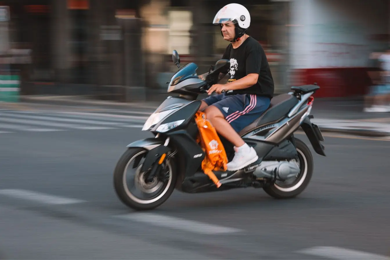 Personne en scooter noir portant casque blanc, image qui illustre la conduite urbaine liée au Permis AM Cyclomoteur.
