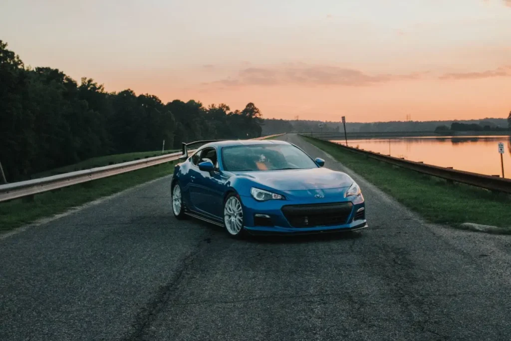 Voiture sportive bleue près d’un lac, symbole des risques mécaniques liés aux ralentisseurs et aux suspensions.