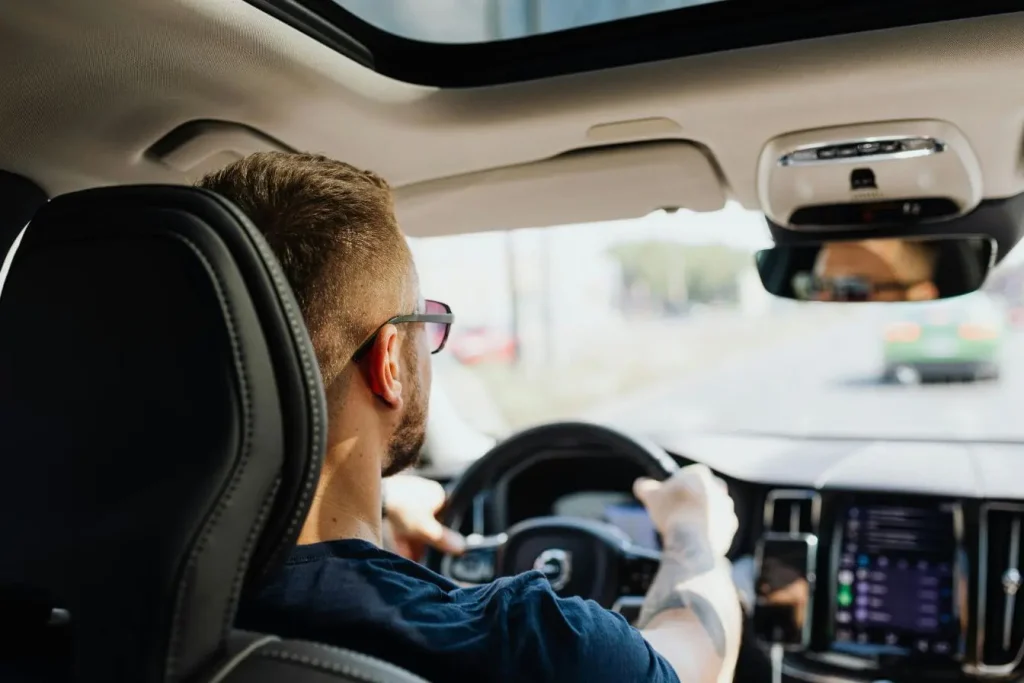 Conducteur portant lunettes au volant d’une berline moderne, image illustrant l’expérience de conduite et la valeur estimée d’une voiture d’occasion.