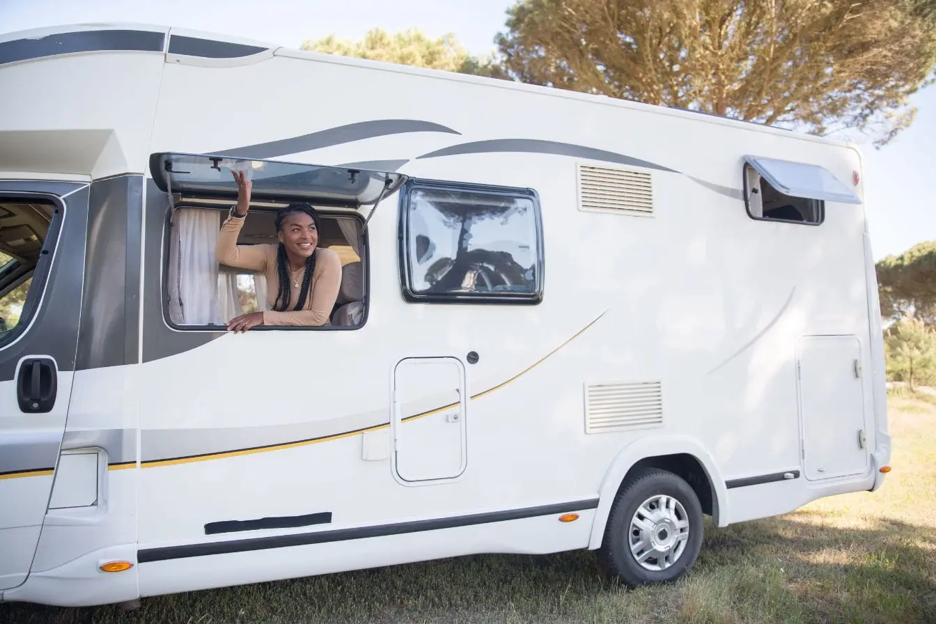camping-car Un camping-car blanc garé sur l’herbe, décoré de bandes grises et jaunes, une personne regarde dehors par la fenêtre, évoquant la liberté de voyager avec permis.