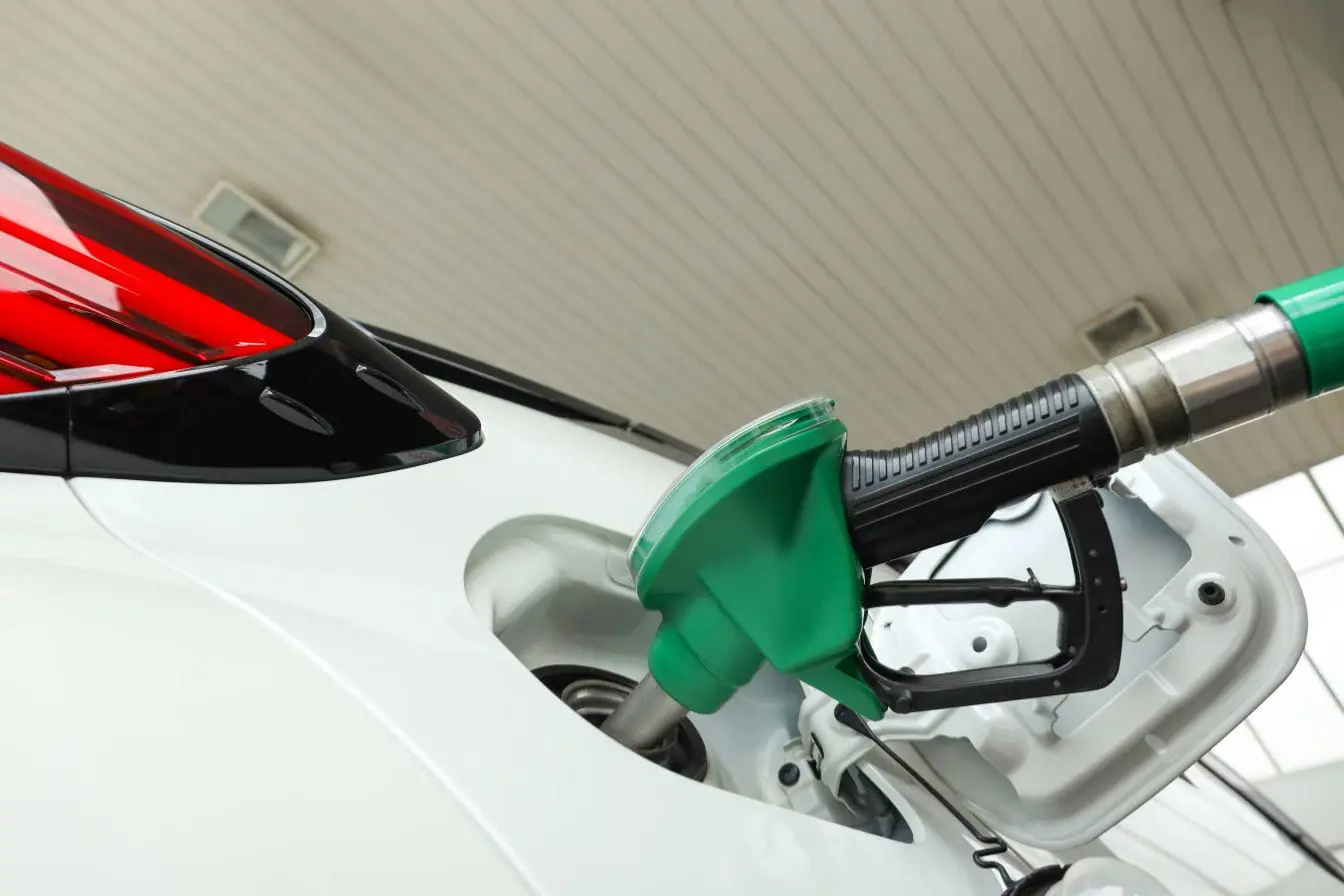 Voiture blanche en station-service avec pistolet vert inséré, image illustrant l’usage d’additifs pour carburant moteur.