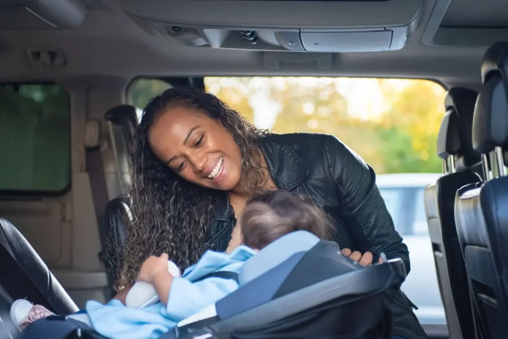 Adulte en veste sombre ajuste bébé installé dans siège auto orienté vers l’arrière, image illustrant la sécurité renforcée du siège dos à la route.