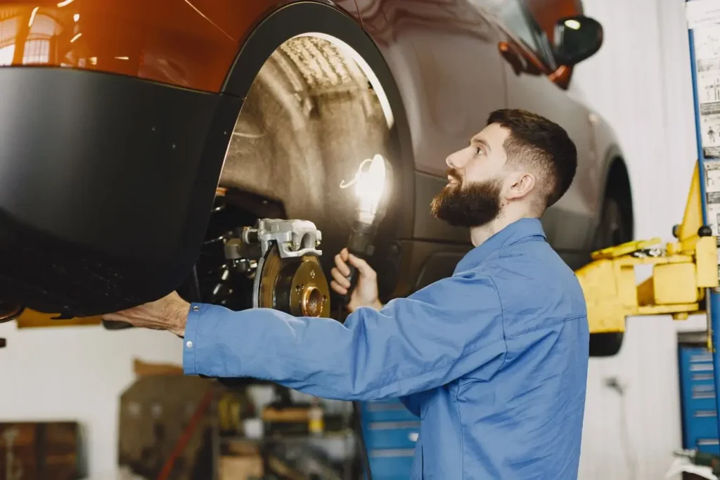 Personne éclaire roue et suspension avec lampe, symbole d’une vérification essentielle lors d’une inspection auto d’occasion.