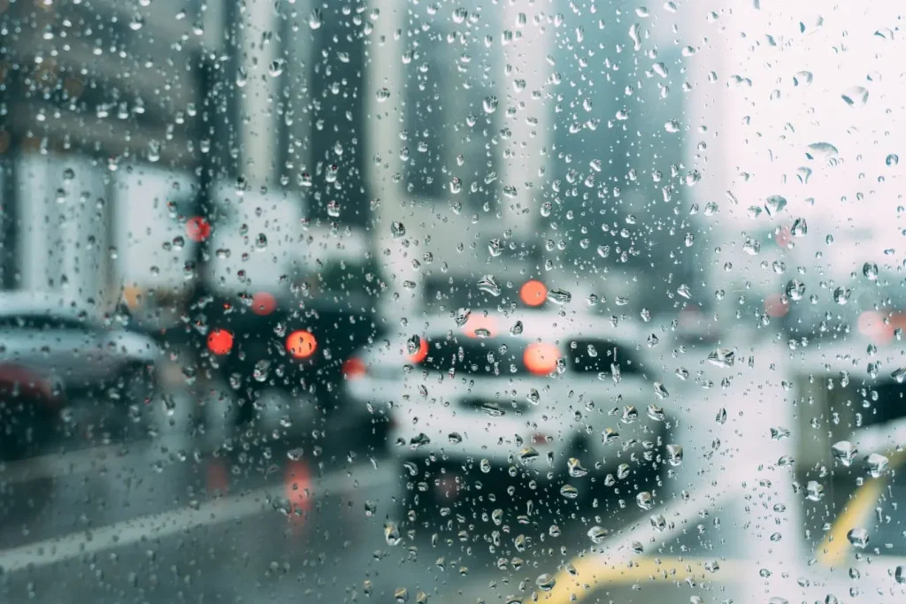 Pare‑brise mouillé avec gouttes visibles et circulation floue, reflet du fonctionnement automatique du capteur de pluie.