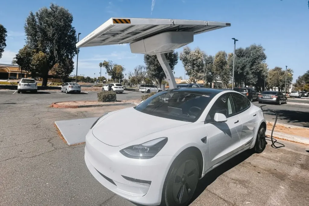 Parking avec borne solaire et Tesla connectée, image qui traduit la recharge d’une voiture électrique via énergie solaire.