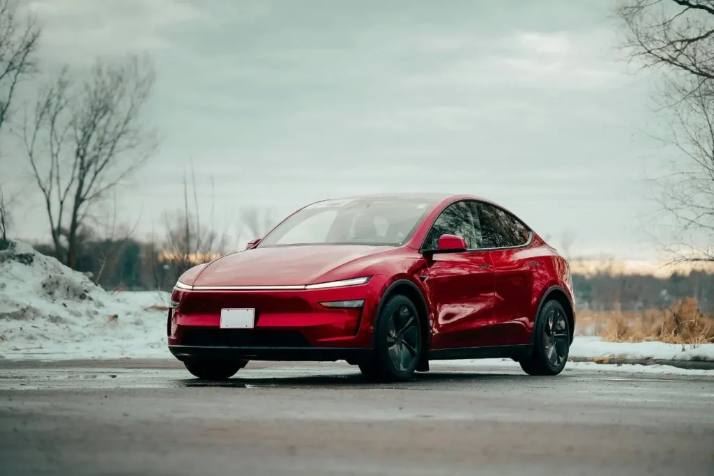Voiture électrique rouge garée sur sol pavé en hiver, image qui illustre l’importance du frein de stationnement électrique dans son usage et son entretien.