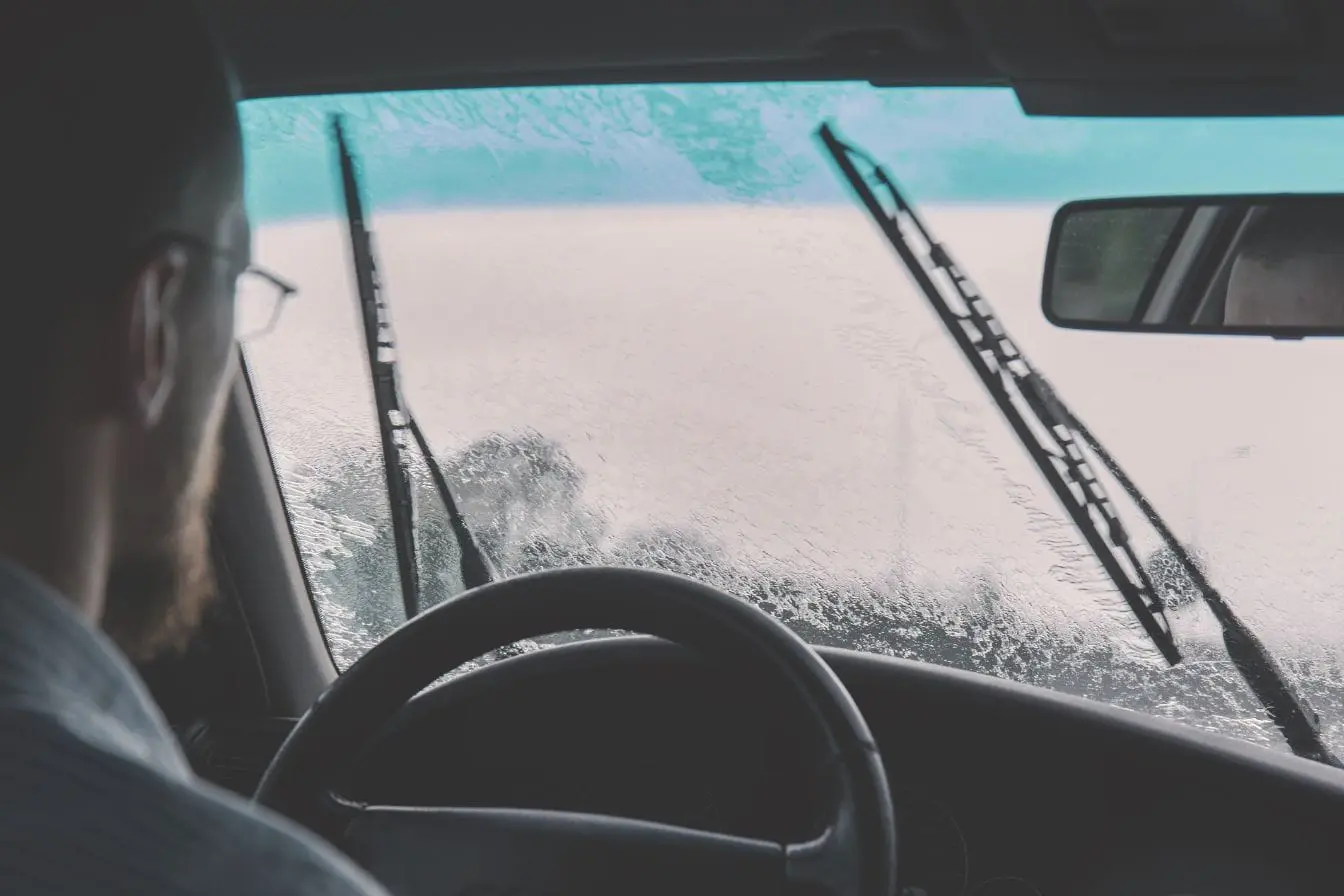Vue intérieure d’une voiture sous la pluie Vue intérieure d’une voiture sous la pluie avec essuie‑glaces en action, image qui illustre le rôle du capteur de pluie pare‑brise.