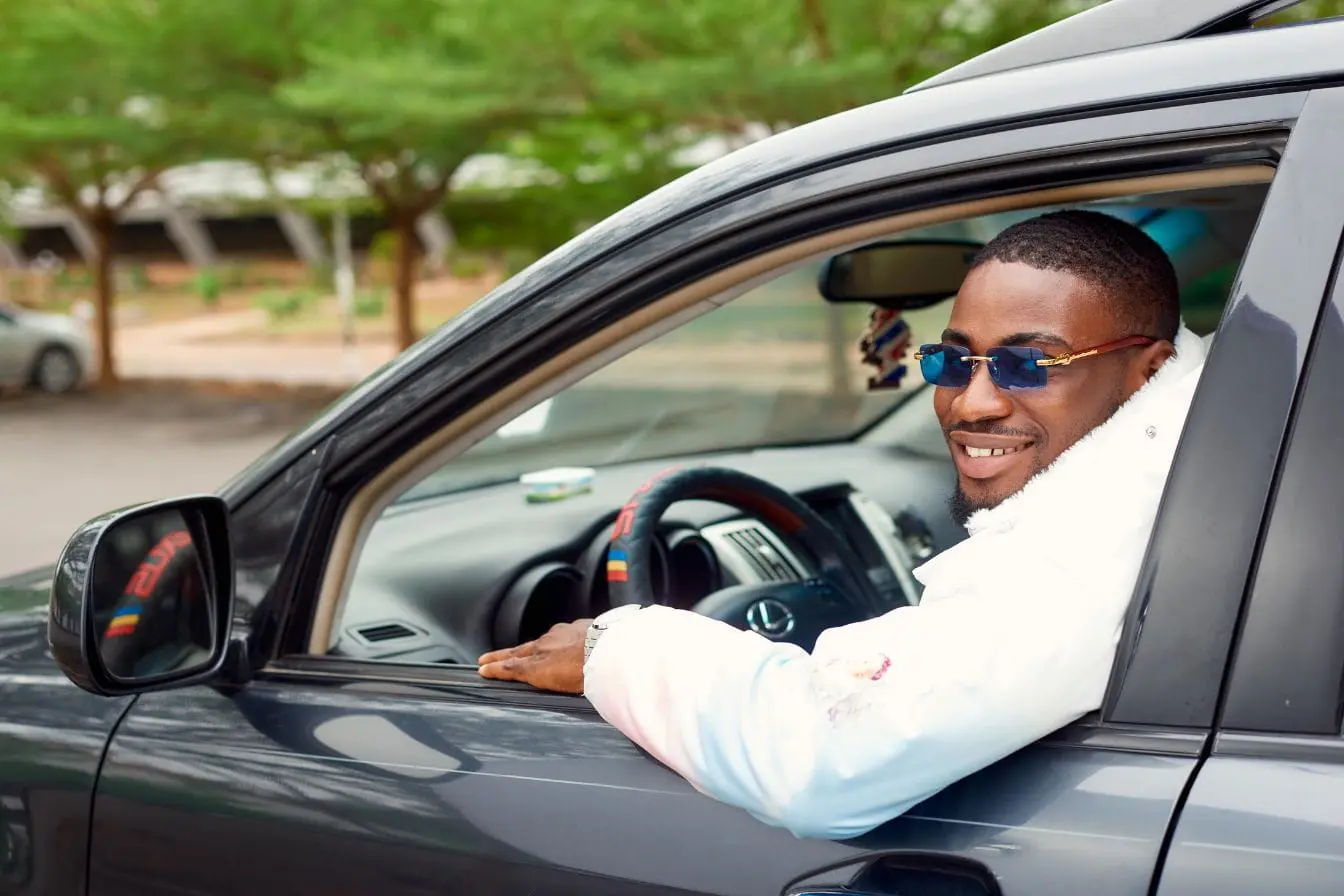 chauffeur de covoiturage Conducteur en veste blanche et lunettes bleues assis au volant, image qui illustre l’idée de devenir chauffeur de covoiturage.