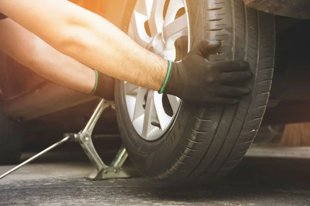 Personne portant des gants change une roue sur voiture soulevée, image qui illustre les méthodes liées au vol automobile en France.