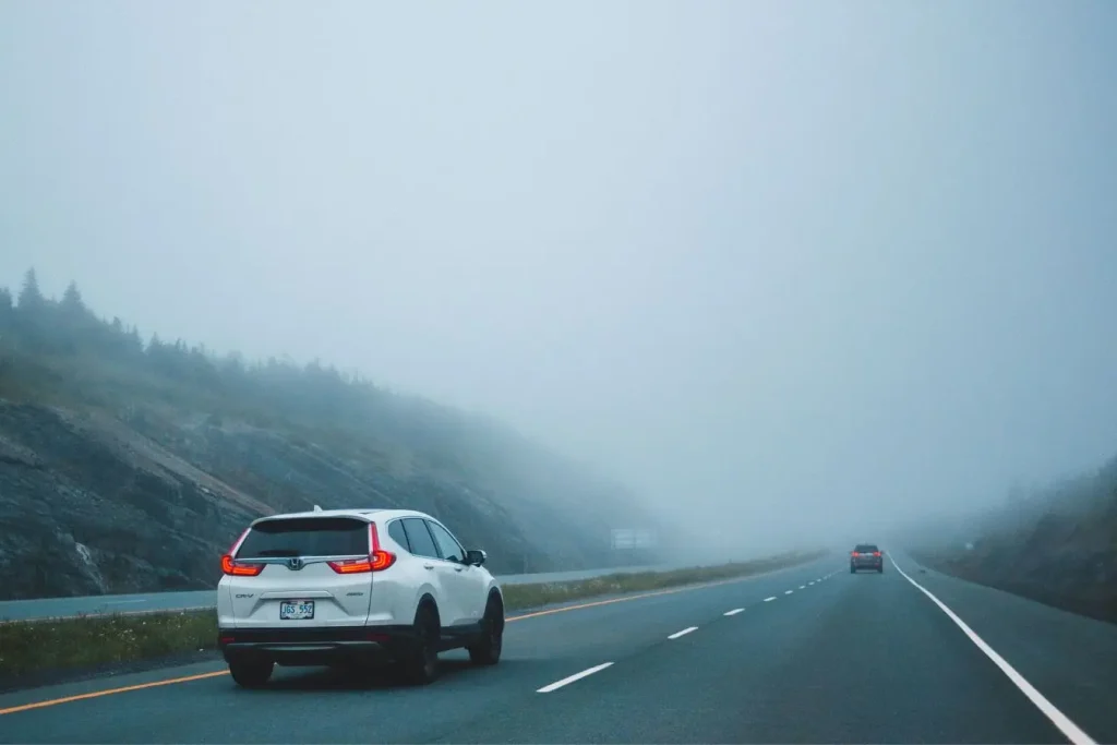 SUV blanc suivi d’un véhicule lointain dans la brume, illustration des conditions de conduite dans le brouillard.