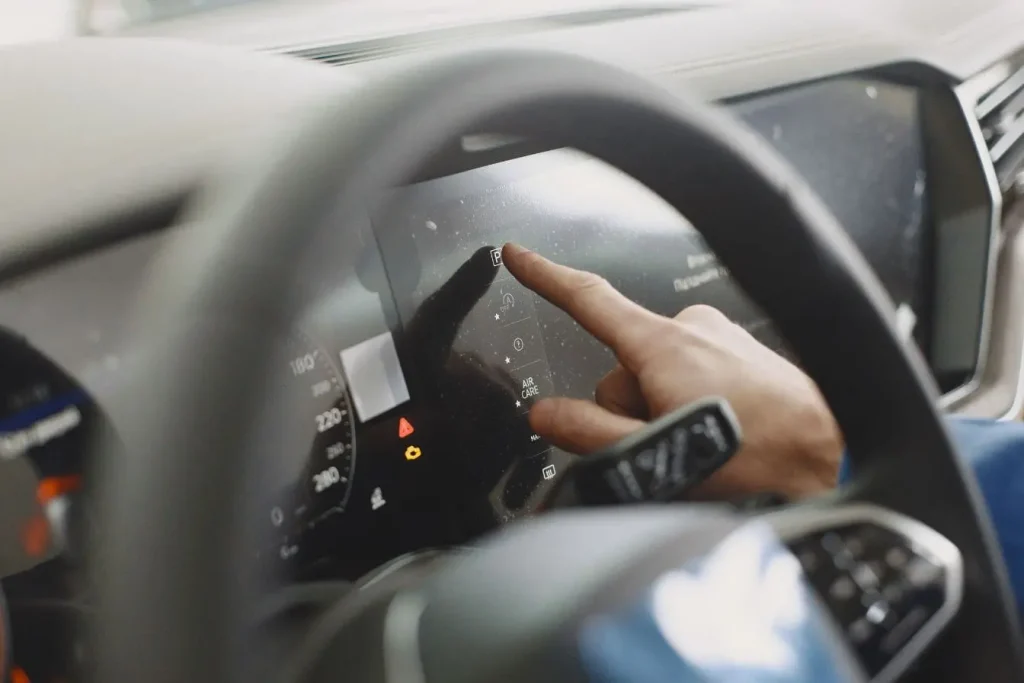 Main appuyant sur écran tactile d’une voiture moderne, image qui illustre l’intégration du HUD pour faciliter la conduite et afficher les informations utiles.