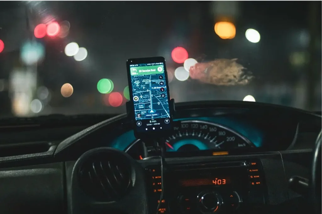 Smartphone fixé sur tableau de bord affichant carte et itinéraire, image qui illustre l’usage d’un traceur GPS pour voiture lors d’un trajet nocturne.