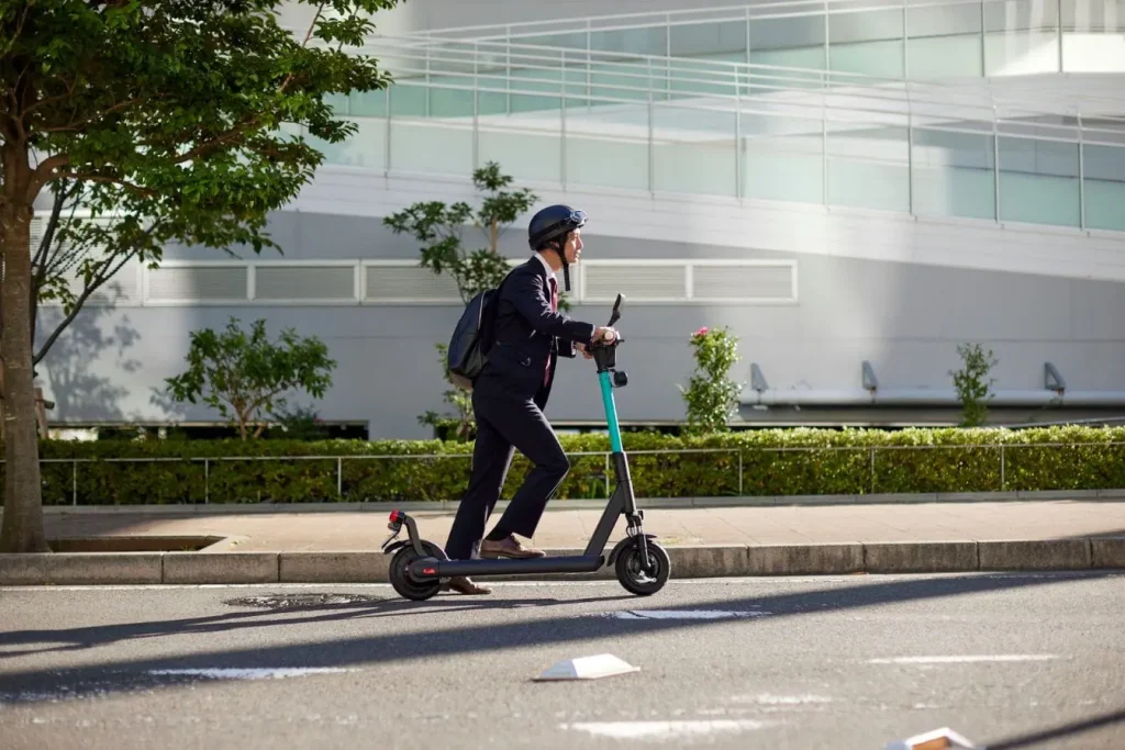 Personne en costume roulant en trottinette électrique noire et turquoise, reflet des règles de circulation publique imposées par la loi en 2026.