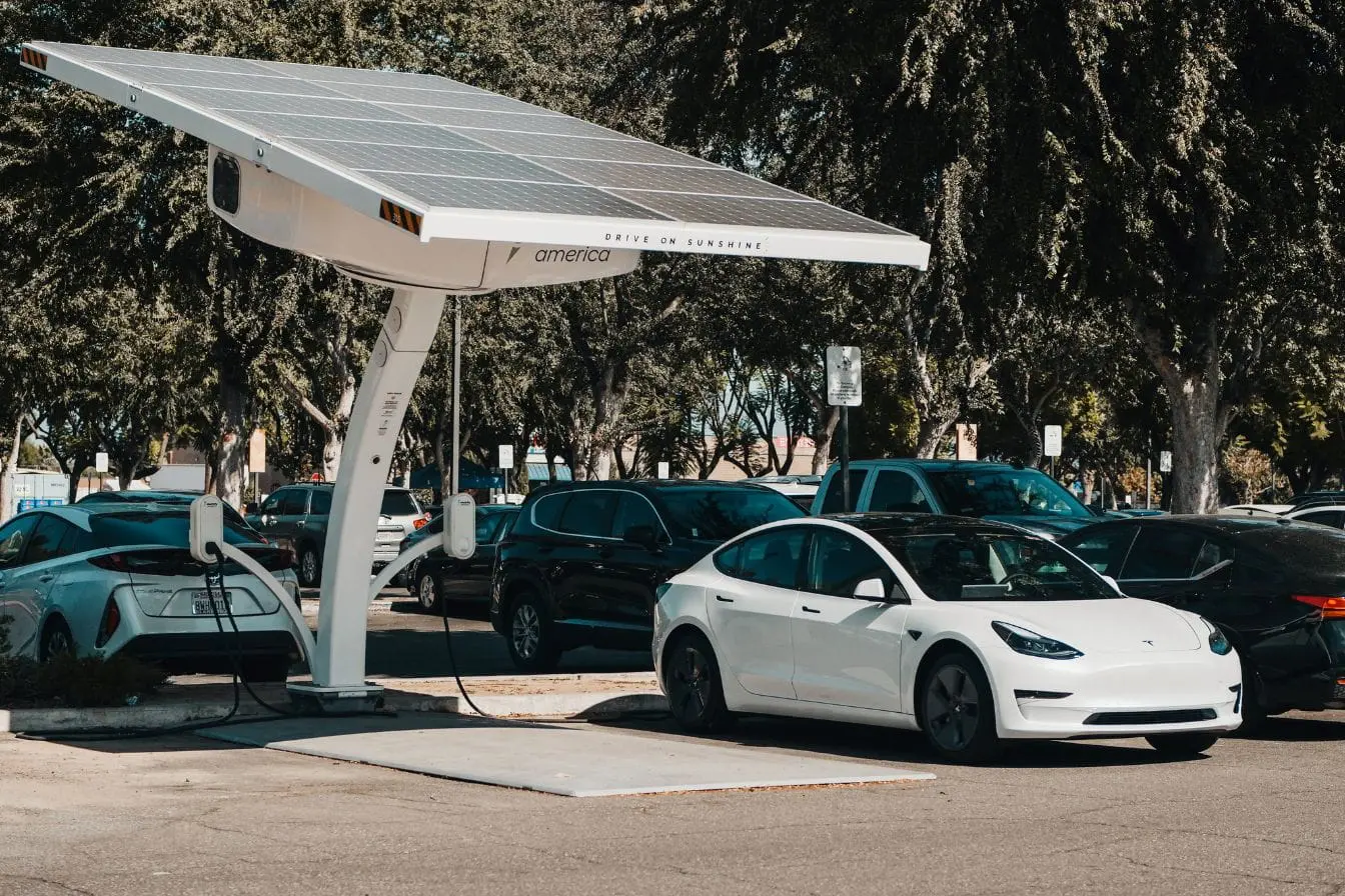 voiture électrique branchée Station solaire avec câbles et voitures garées, illustration de l’usage du frein de stationnement électrique.