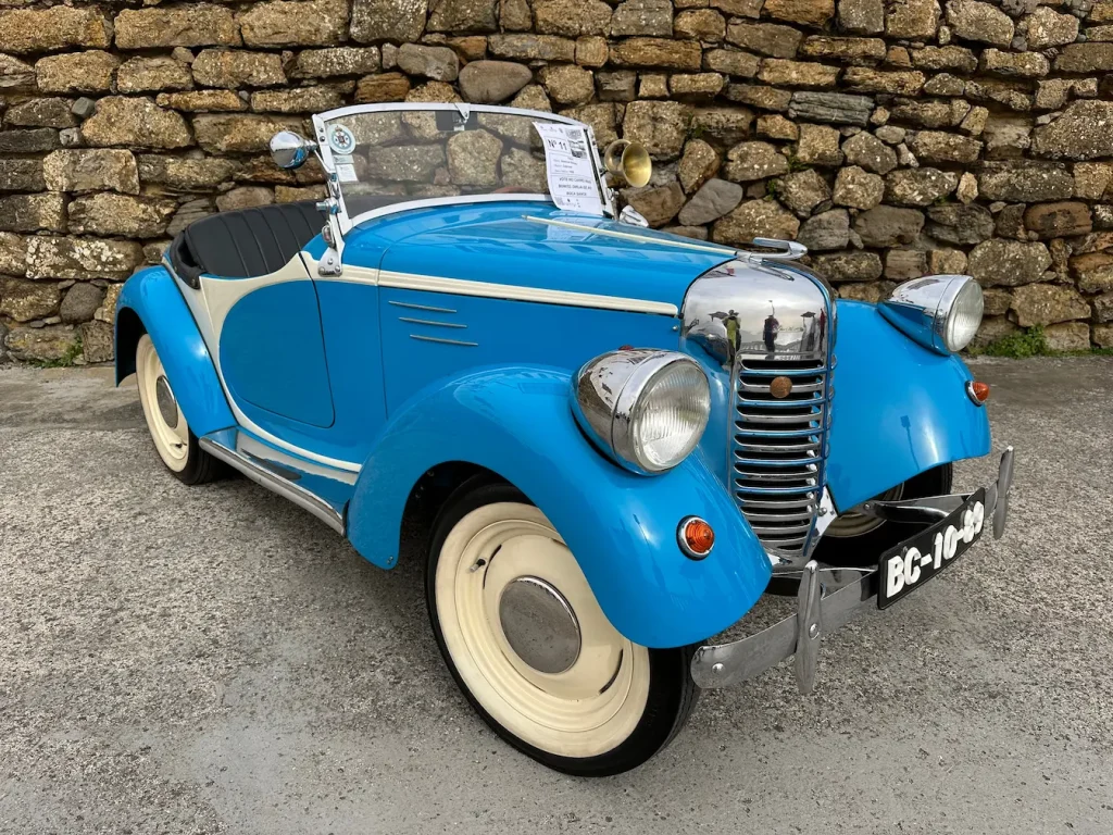 Cabriolet bleu et blanc vintage garé devant un mur de pierre, image qui illustre véhicule ancien et carte grise collection avantages et démarches.