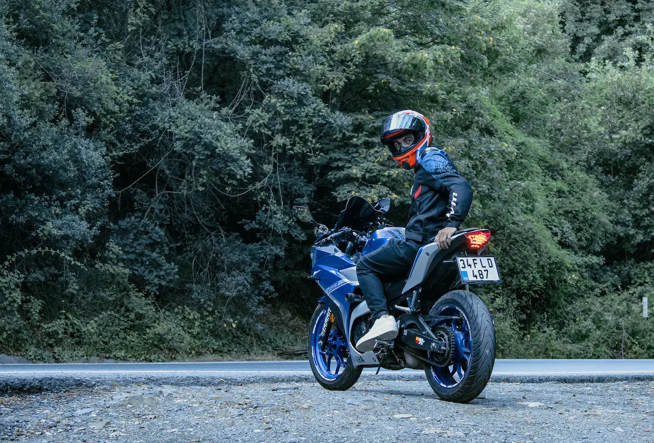 Motard en casque noir assis sur moto bleue garée, image qui illustre passer du permis A2 au permis A sans examen.