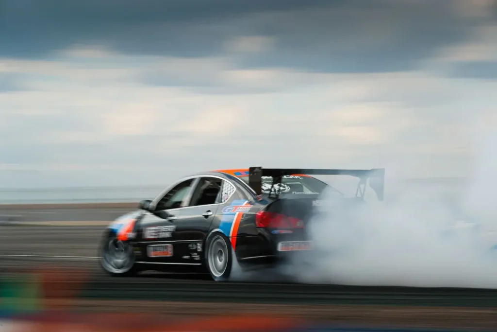 Voiture de course noire et orange dérivant sur piste, reflet d’un roulage privé nécessitant organisation et règles de sécurité.
