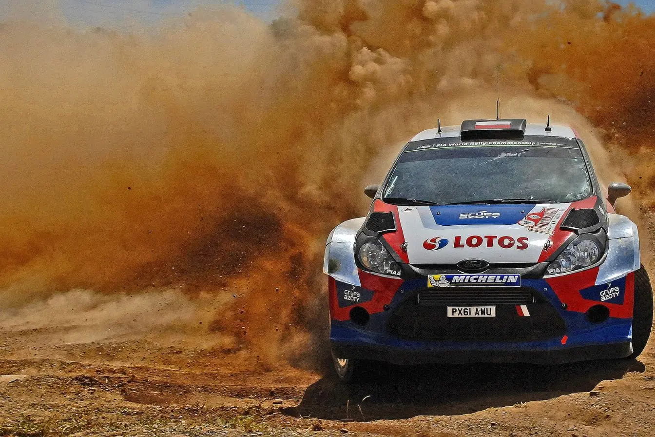 Voiture de rallye Ford décorée logos sponsors soulevant nuage de poussière, reflet de l’intensité du WRC face aux différences avec WRC2.